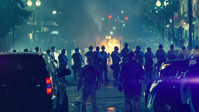 Lockjaw looks on as riot police stand in the streets in One Battle After Another