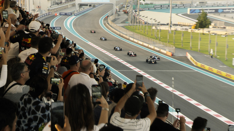 Formula 1 cars are racing around a path while fans watching stands in F1: The Movie