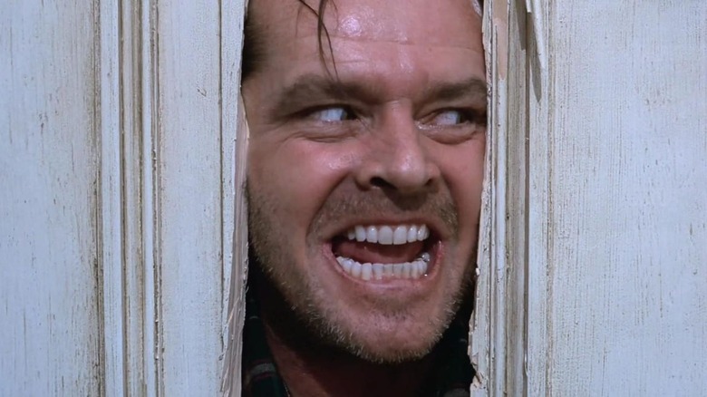 Jack (Jack Nicholson) grins evilly with his face in between the hole of a broken door in The Shining