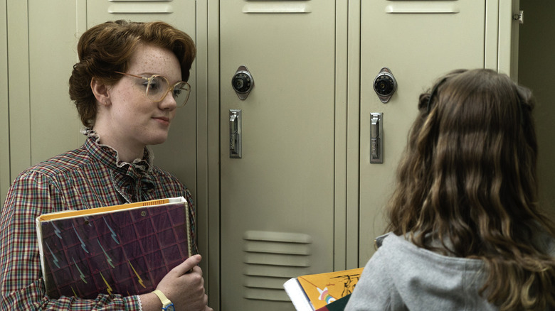 Barb talking to Nancy by their high school lockers in the hall in Stranger Things