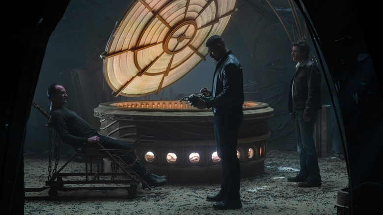 Ulrich Thomsen's Thaal Sinestro sits in a chair as Aaron Pierre's John Stewart and Kyle Chandler's Hal Jordan watch in Lanterns.jpg.jpg