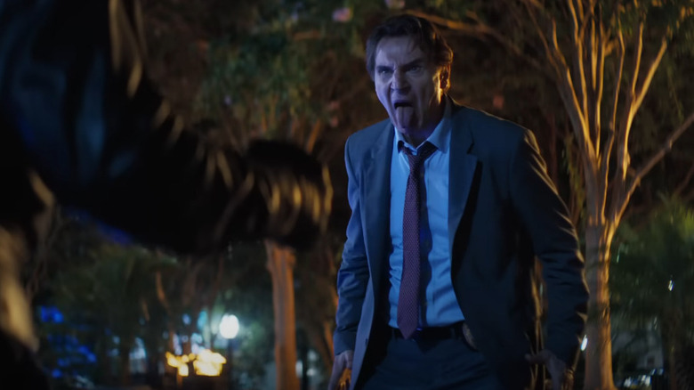 Liam Neeson as Frank Drebin sticking his tongue out while confronting a criminal in a park at night in The Naked Gun (2025)