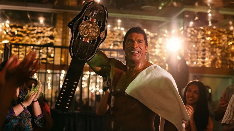 Dwayne Johnson as Mark Kerr hoists a championship belt in The Smashing Machine