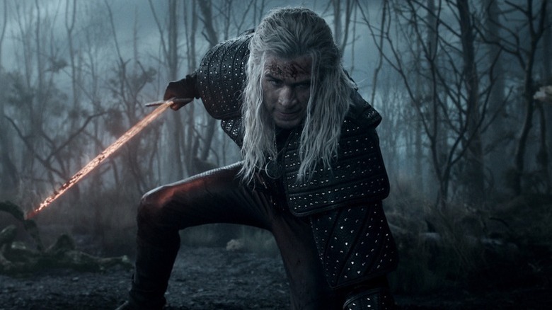 Geralt (Liam Hemsworth) kneels in a swamp while holding a heated sword in The Witcher