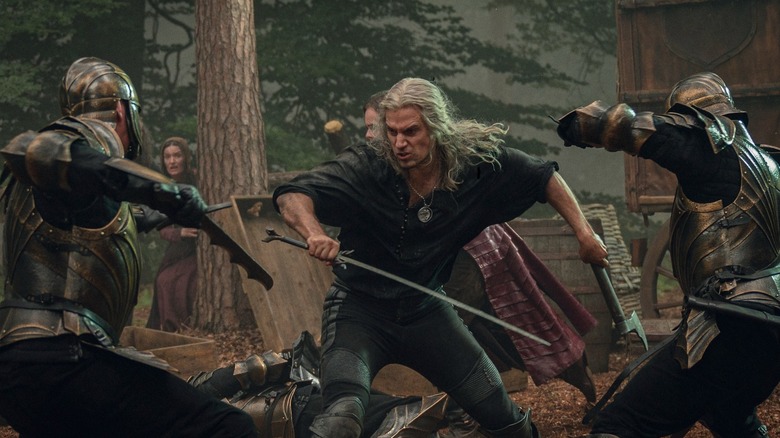 Geralt (Henry Cavill) fights two soldiers in a forest in The Witcher