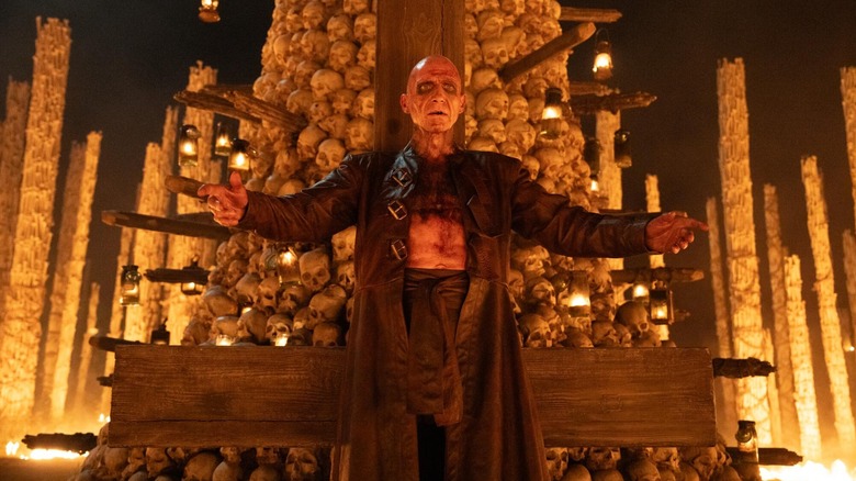 Dr Ian Kelson about to do the sickest rock performance in English history with a massive pile of skulls behind him in 28 Years Later: The Bone Temple