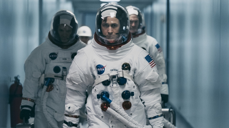 Ryan Gosling as Neil Armstrong walking down a corridor in an astronaut suit ahead of Lukas Haas as Mike Collins and Corey Stoll as Buzz Aldrin in First Man