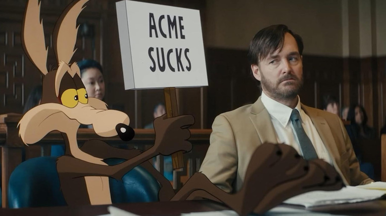 Wile E. Coyote holding up a sign that reads 'Acme sucks' next to Will Forte as Kevin Avery in Coyote vs. Acme
