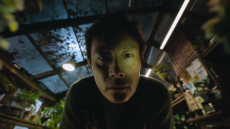 Lee Byung-hun as Yoo Man-su staring directly into the camera with a fish-eye lens in the greenhouse in No Other Choice