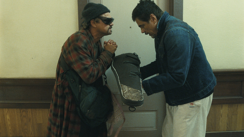Benicio del Toro as Sensei St. Carlos bowing to Leonardo DiCaprio as Bob Ferguson in a hallway in One Battle After Another