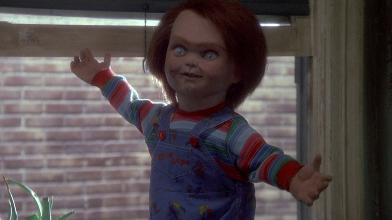 Chucky (Brad Dourif) stands with his arms outstretched by a window in Child's Play (1988)