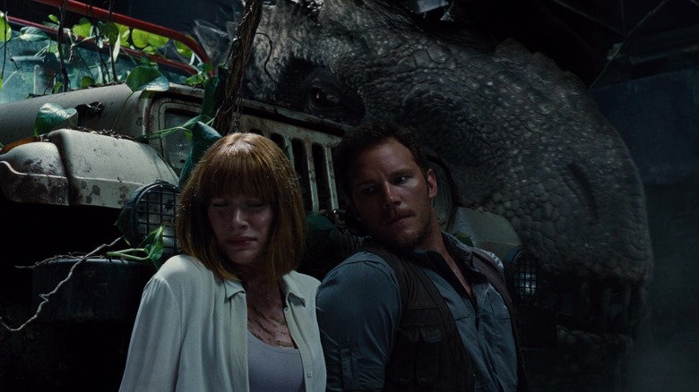 Claire and Owen hiding from a giant dinosaur behind a jeep in Jurassic World