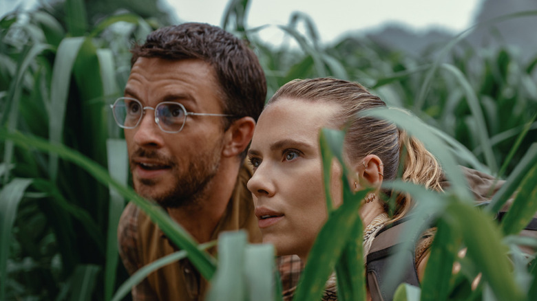 Dr. Loomis and Zora hiding in the grass in Jurassic World Rebirth