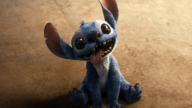 Stitch sits on the ground with his tongue hanging out of his mouth and a big toothy grin in 