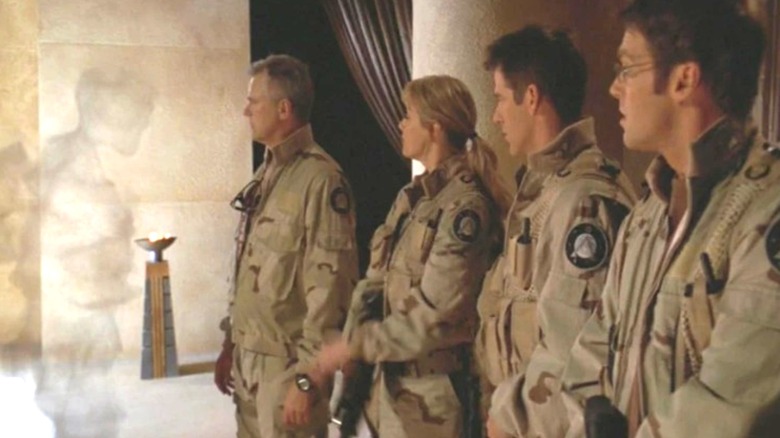 Richard Dean Anderson as Jack O'Neill, Amanda Tapping as Samantha Carter, Ben Browder as Cameron Mitchell, and Michael Shanks as Daniel Jackson looking at a vanishing silhouette in Stargate: Continuum