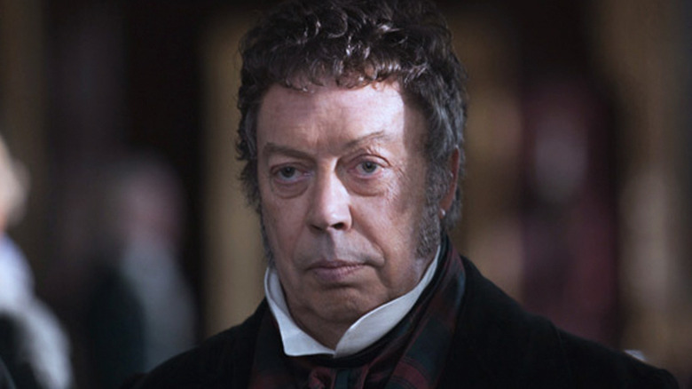 Tim Curry's Alexander Monro is seen in closeup in Burke & Hare with a blank stare on his face