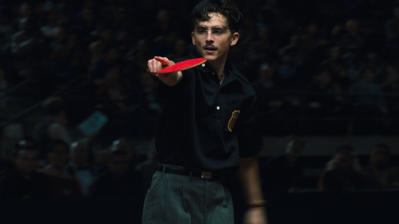 Timothée Chalamet as Marty Mauser holding up a paddle and pointing during a ping pong match in Marty Supreme