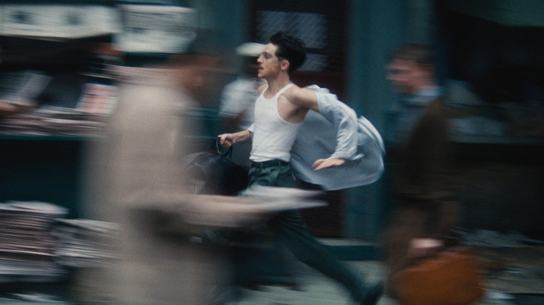 Timothée Chalamet as Marty Mauser running through the streets of New York City with a bag in hand in Marty Supreme