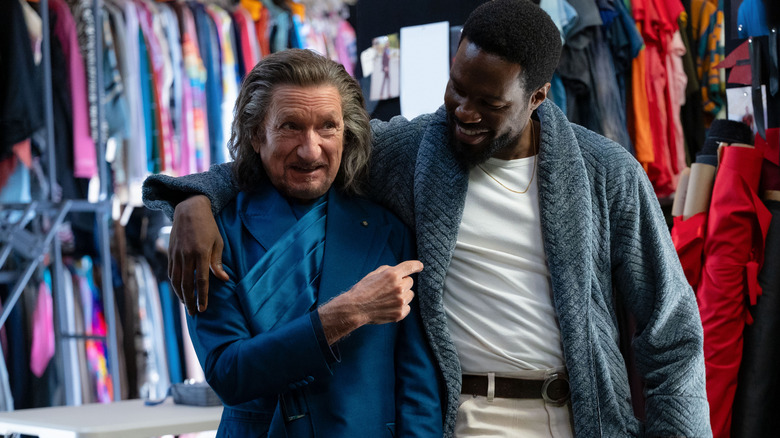 Sir Ben Kingsley as Trevor Slattery wearing an expensive suit and sharing an embrace with Yahya Abdul-Mateen II as Simon Williams in Wonder Man