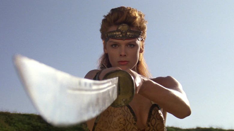 Brigitte Nielsen as Red Sonja (1985) pointing a curved sword at the camera
