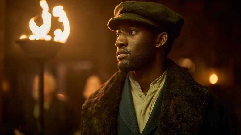 Malachi Kirby as Hezekiah Moscow standing outside in front of a flaming torch at nighttime in A Thousand Blows