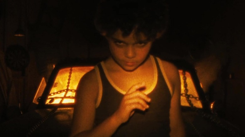 A young boy looking creepy in front of a burning car in Sinister