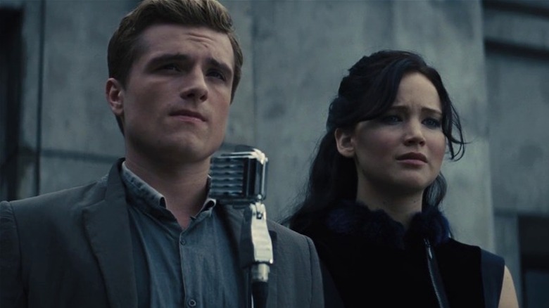 Peeta Mellark and Katniss Everdeen standing in front of a microphone on a stage