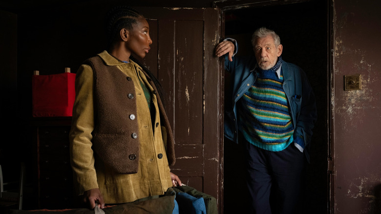 Ian McKellen as Julian Sklar standing by a doorway opposite Michaela Coel as Lori Butler in The Christophers
