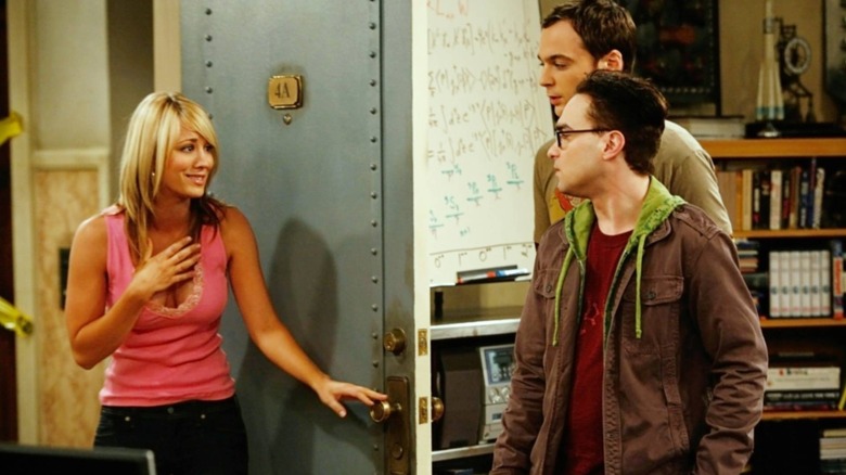 Kaley Cuoco as Penny standing by the door of an apartment in front of Jim Parsons as Sheldon Cooper and Johnny Galecki as Leonard Hofstadter in The Big Bang Theory