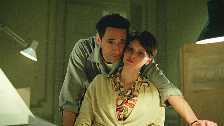 László Tóth leaning over his wife Elisabeth in The Brutalist