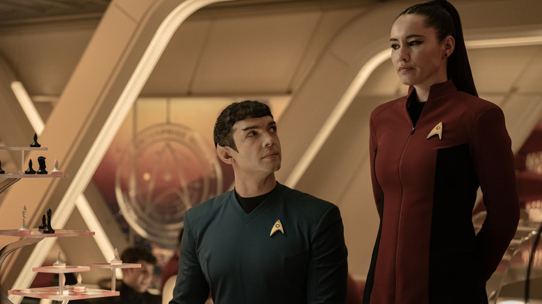 Ethan Peck as Spock sitting at a table and looking up at Christina Chong as La'an Noonien-Singh standing next to him in Star Trek: Strange New Worlds