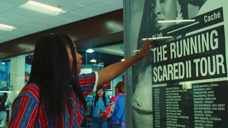 Dominique Fishback as Dre admiring a Ni'jah Running Scared Tour poster in Swarm