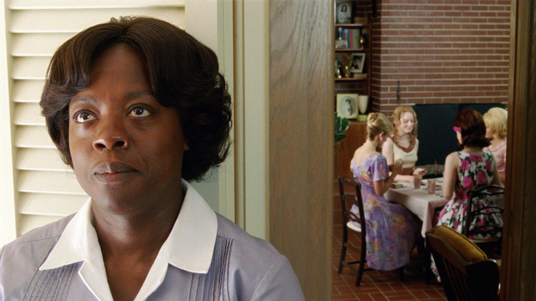 Aibileen leaning against a door while Skeeter and her friends play cards in The Help