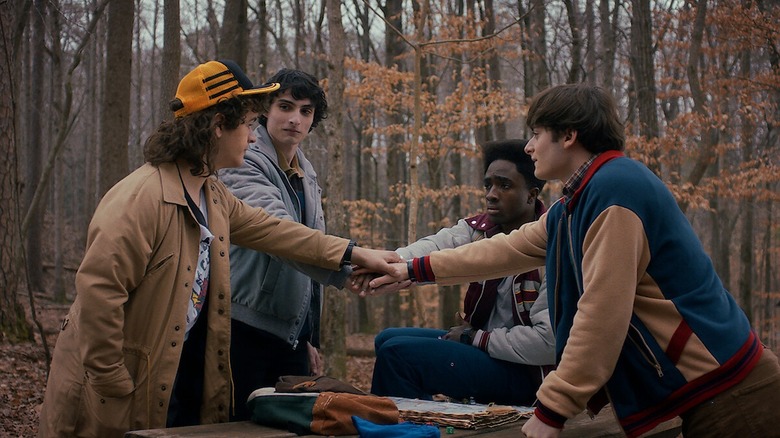 Dustin, Mike, Lucas, and Will touching hands in a circle in Stranger Things season 5