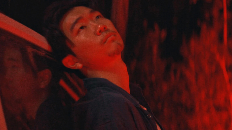 James leans against the back of a Jeep and stares into the night sky as he's bathed in red light in It Ends