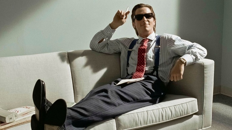 Patrick Bateman in American Psycho sitting on a couch with sunglasses on