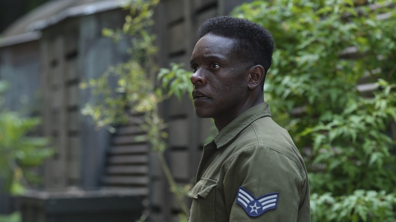 Chris Chalk as Dick Hallorann standing in front of a building and green plants in It: Welcome to Derry