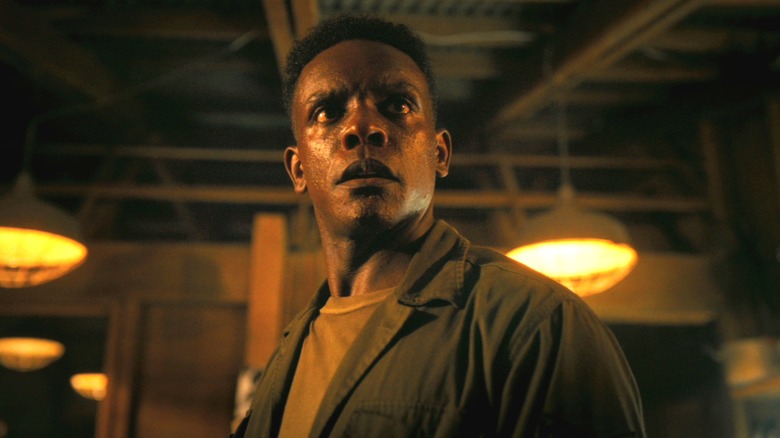 Chris Chalk as Dick Hallorann standing in a warehouse and looking concerned at something off-screen in It: Welcome to Derry