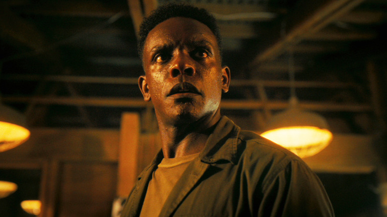 Chris Chalk's Dick Hallorann looks worried as he stands in a dimly lit room in It Welcome to Derry