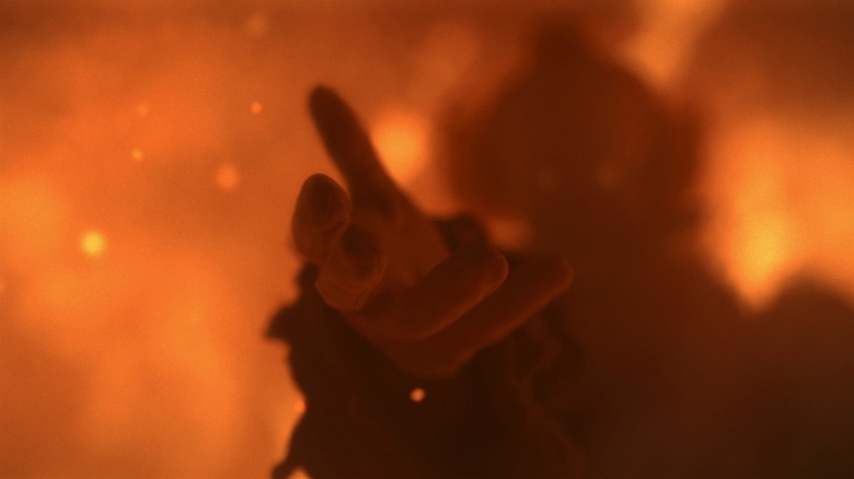 Bill Skarsgård as Pennywise the Clown extending its hand amidst flames on It: Welcome to Derry