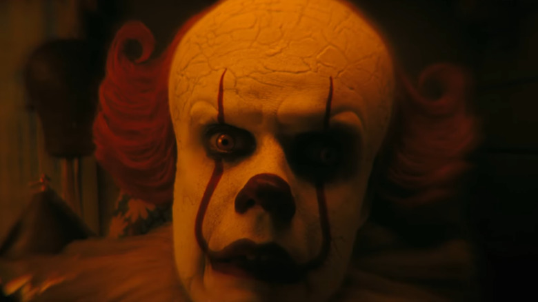 Bill Skarsgård as Pennywise bathed in orange light and looking confused in It: Welcome to Derry