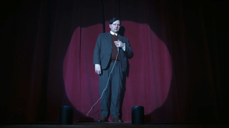 Robert Clarke's Principal Dunleavy is on stage with a microphone in It Welcome to Derry