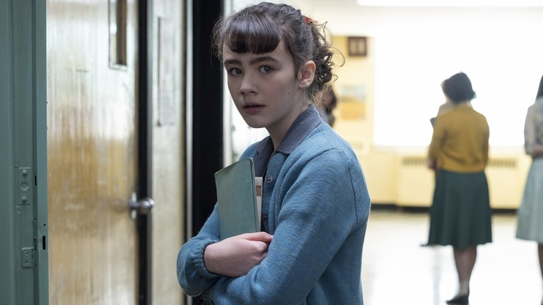Lily (Clara Stack) holding a stack of books in a hallway in It: Welcome to Derry