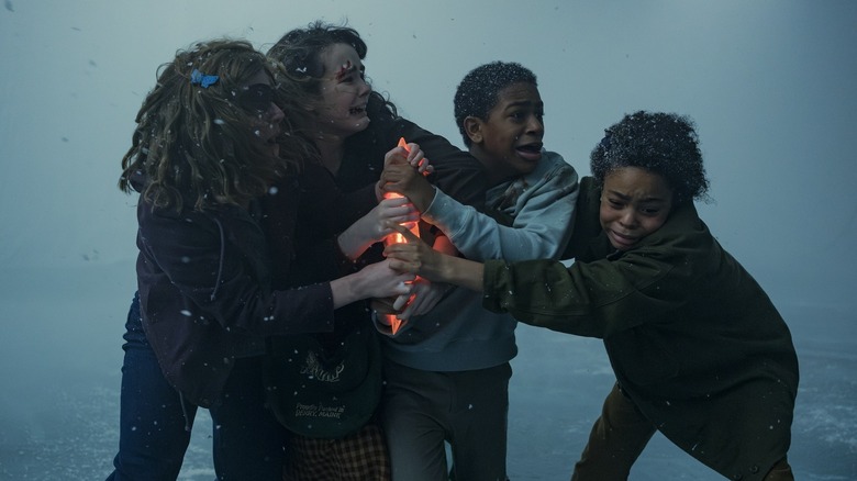 Matilda Lawler as Marge Truman holding onto a glowing object next to Clara Stack as Lilly Bainbridge, Blake Cameron James as Will Hanlon, and Amanda Christine as Ronnie Grogan in a snowstorm in It: Welcome to Derry