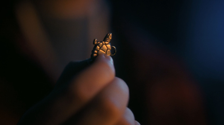A hand holds up a turtle charm in closeup in Welcome to Derry