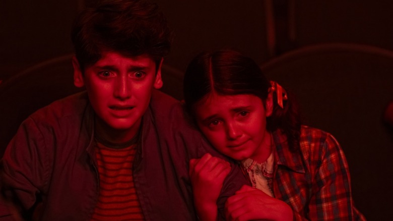 Jack Molloy Legault's Phil Malkin and Matilda Legault's Susie Malkin cower while illuminated in red light in It: Welcome to Derry