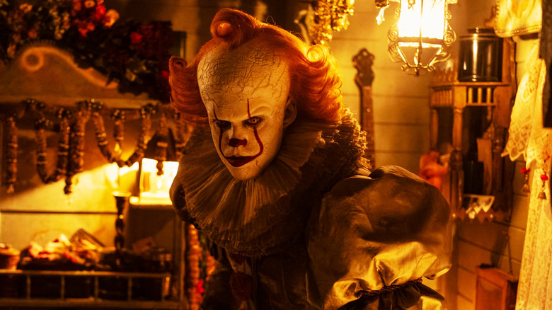 Bill Skarsgård's Pennywise stands inside a warmly lit room in It Welcome to Derry