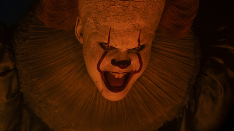 Bill Skarsgård's Pennywise looks angry as he's bathed in orange light in It Welcome to Derry