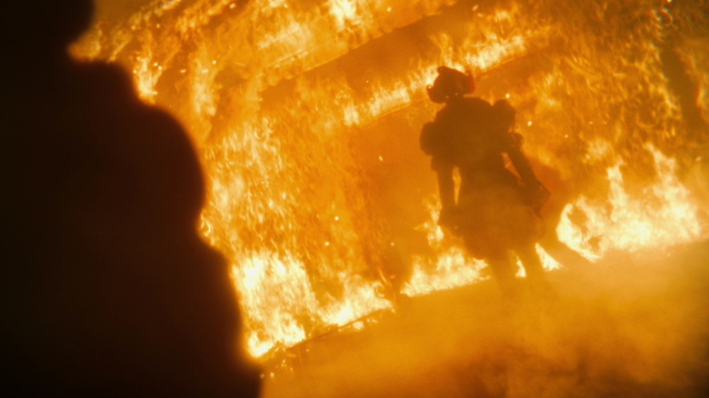 Bill Skarsgård's Pennywise stands in the middle of the Black Spot bar as it burns in It Welcome to Derry