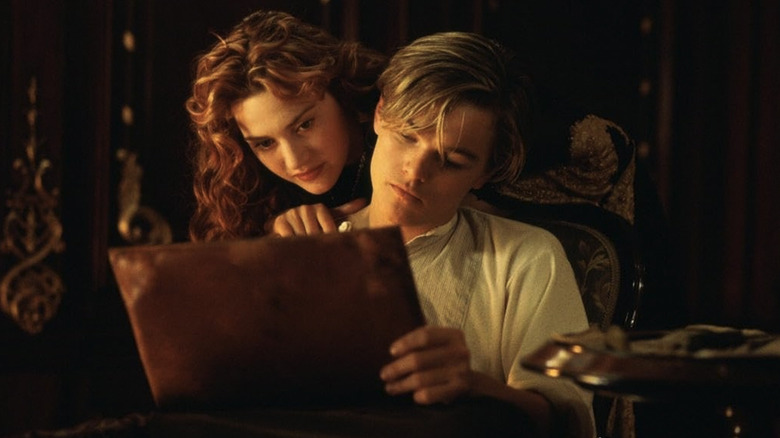 Rose leaning over Jack's shoulder as she watches him sketch in his notebook in Titanic
